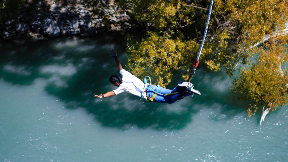 A man is hanging from a zip line over a river.