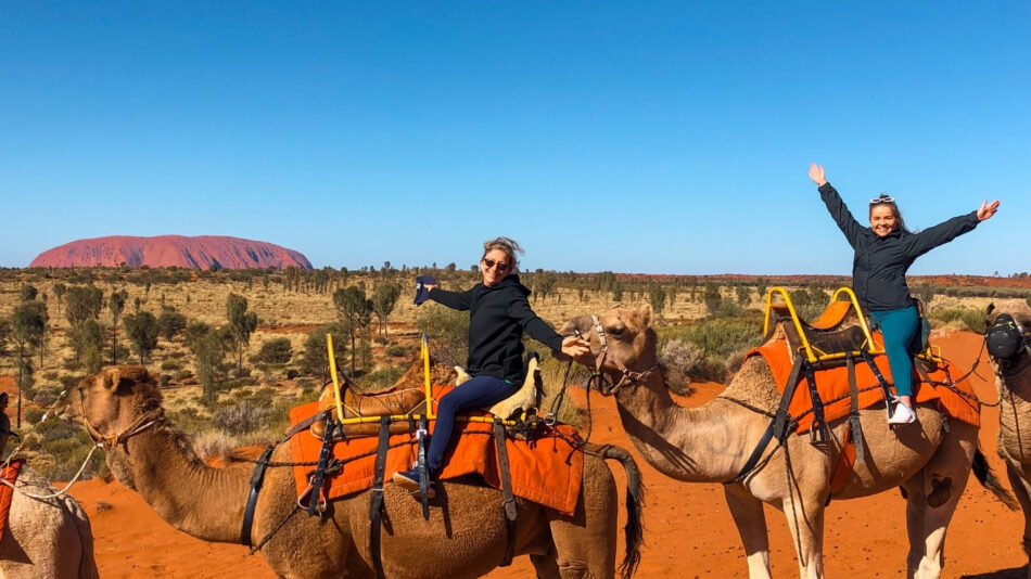 Two women on camels explore Uluru during their gap year.