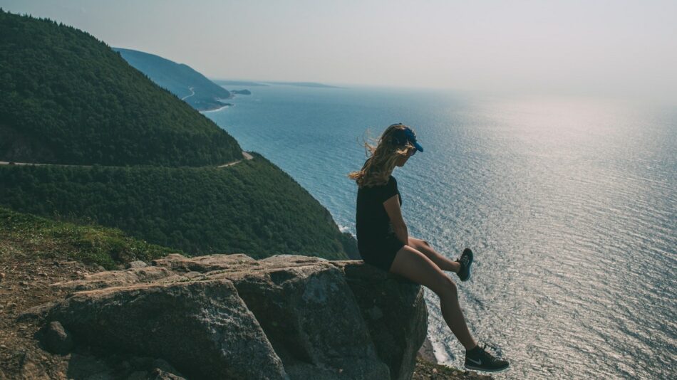 A woman sitting on a cliff overlooking the ocean.