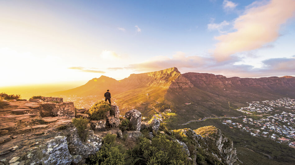 A man standing on top of a mountain overlooking a city.