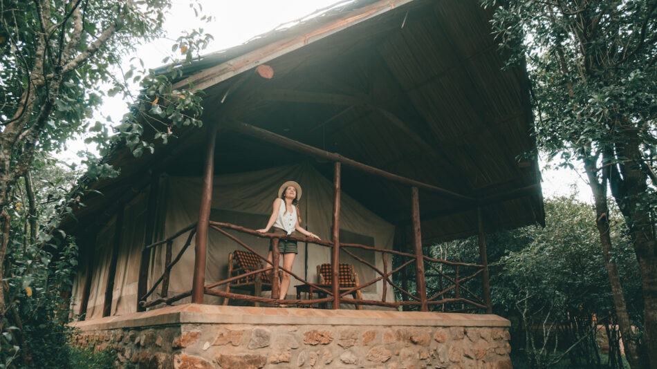 A woman standing on the porch of a wooden cabin in the woods.