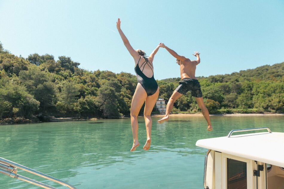 Two people participating in Croatia festivals, jumping off a boat into the water.