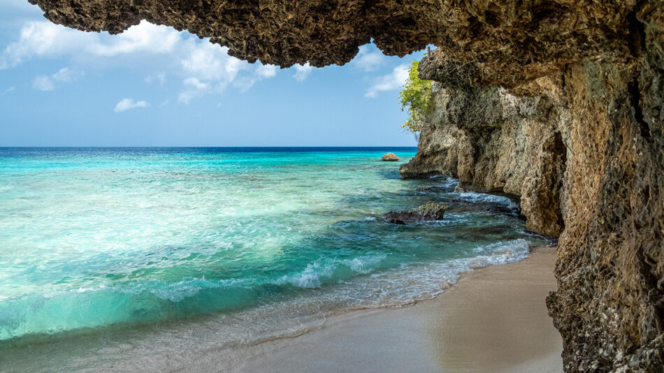 A cave with a sandy beach and blue water, one of the best places to visit in August.