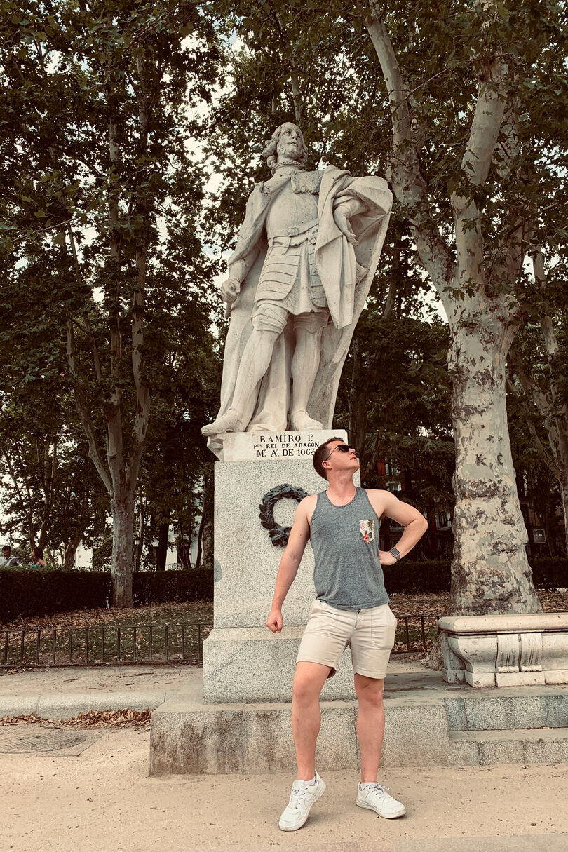 A man, Dom Oliver, standing next to a statue in a park.