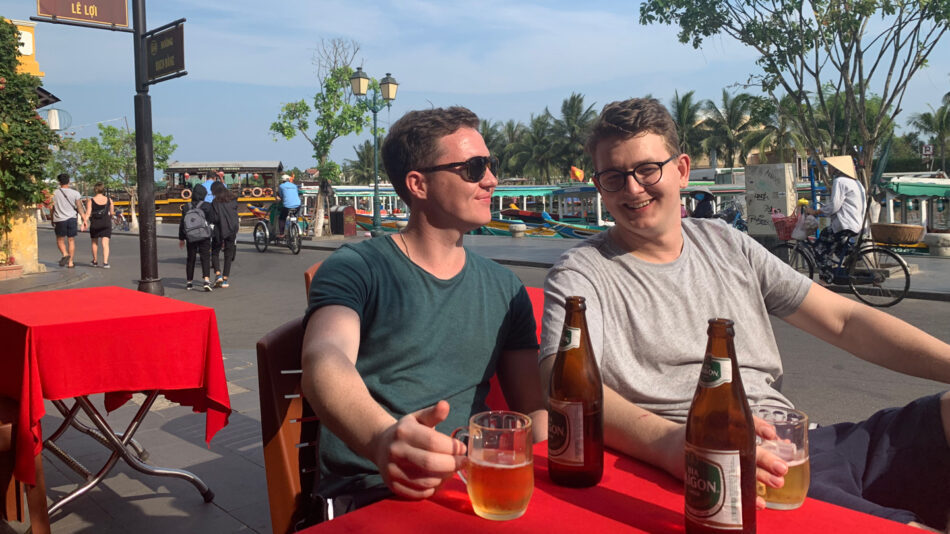 Two men, Dom and Oliver, sitting at a table with beer bottles.