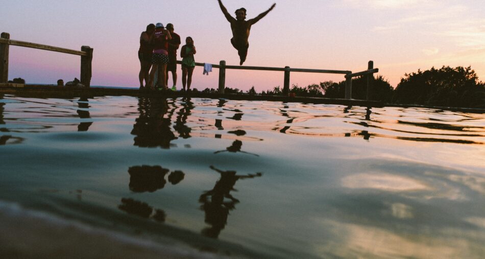 A group of people enjoying a digital detox by jumping into a pool at sunset.