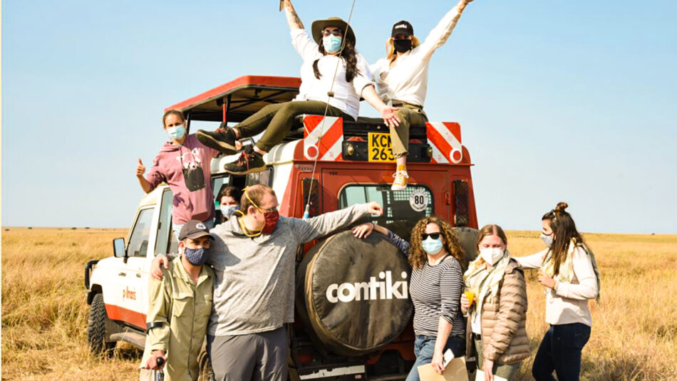 A group of people standing on top of a truck during an African safari experience in the middle of a field.