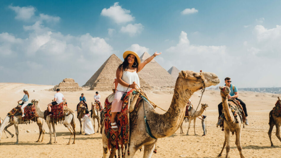 A woman riding a camel in front of pyramids, showcasing her adventurous travel experience in Egypt.