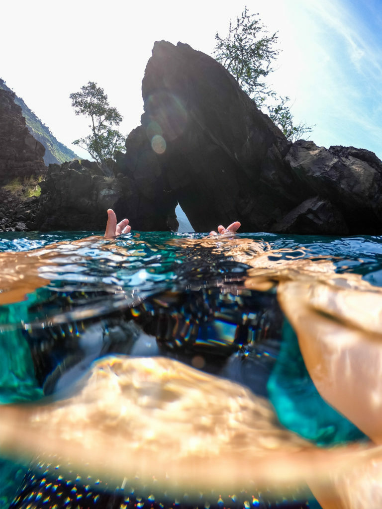 A person is swimming near a rock in Hawaii.