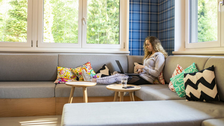 A woman sitting on a couch using a laptop at Gasthof Schoneck.