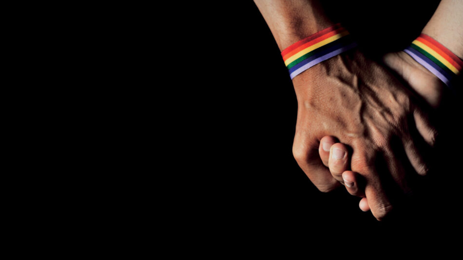 Two people holding hands with rainbow ribbons on them.