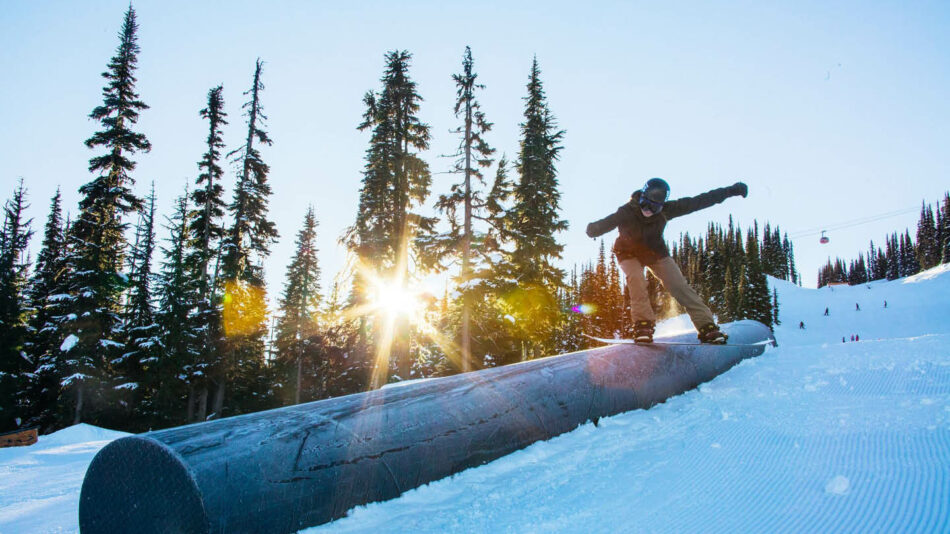 A snowboarder is riding down a log on a group ski trip in the snow.