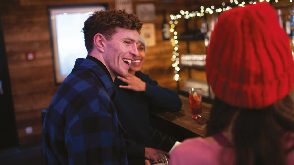 A group of people laughing at a bar during a ski trip.