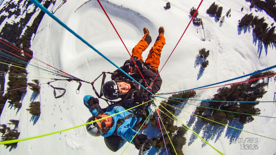 Two people enjoying a exhilarating paragliding adventure during their group ski trip in the snowy mountains.