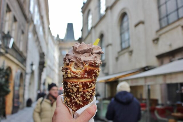 A person holding an ice cream cone in front of a building in Prague.