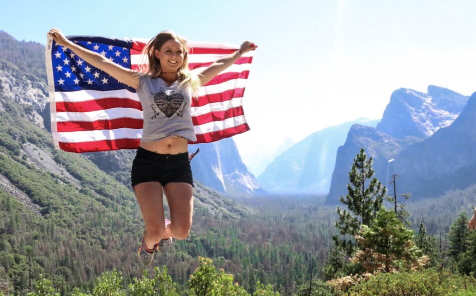 A woman on the west coast is jumping up and down with an American flag.