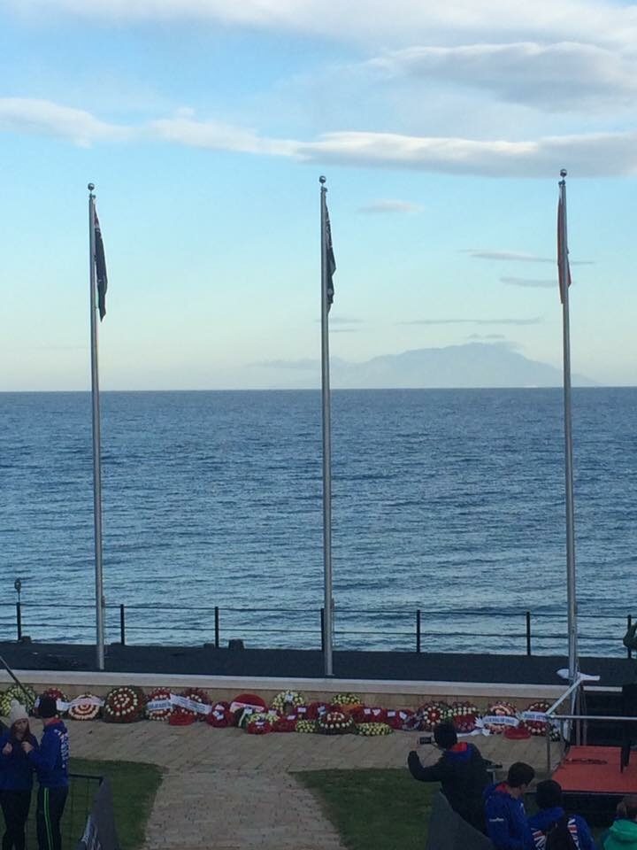 A group of people standing in front of the ocean with Anzac Day flags.