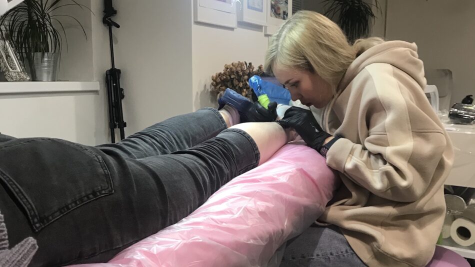 A woman getting an eco-friendly tattoo on her leg, as a unique travel souvenir.