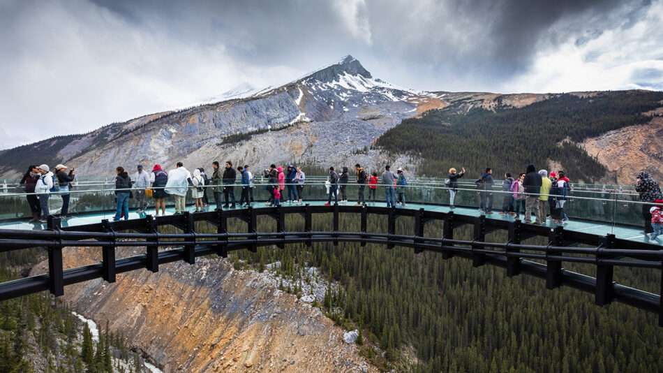 A group of people standing on a glass bridge overlooking a mountain.