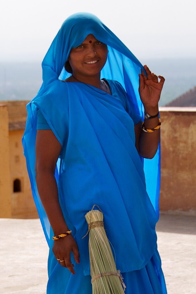 A posed woman in a blue sari holding a broom.