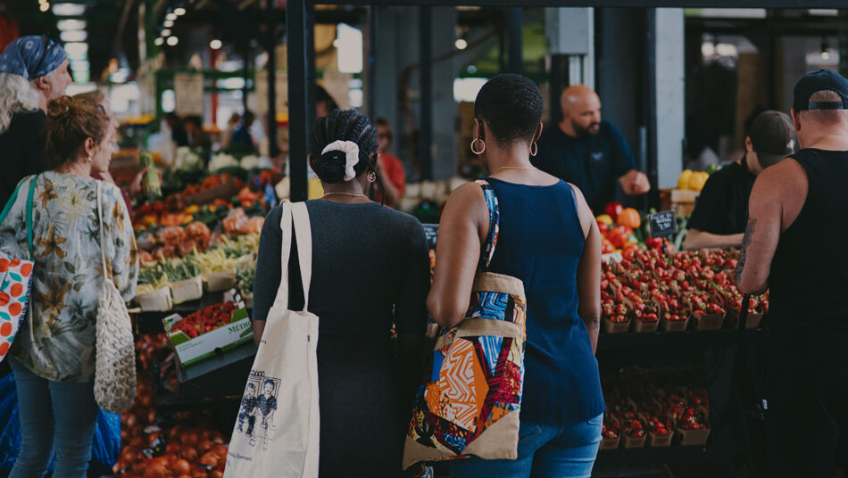 A vibrant gathering of people exploring and purchasing fresh produce and artisanal goods at a bustling farmers' market, one of the best places to visit in August for a delightful shopping experience.