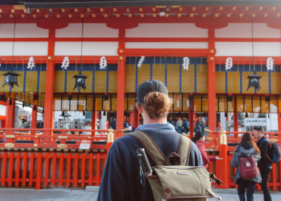 A man with a backpack standing in front of an Asian temple in Japan.