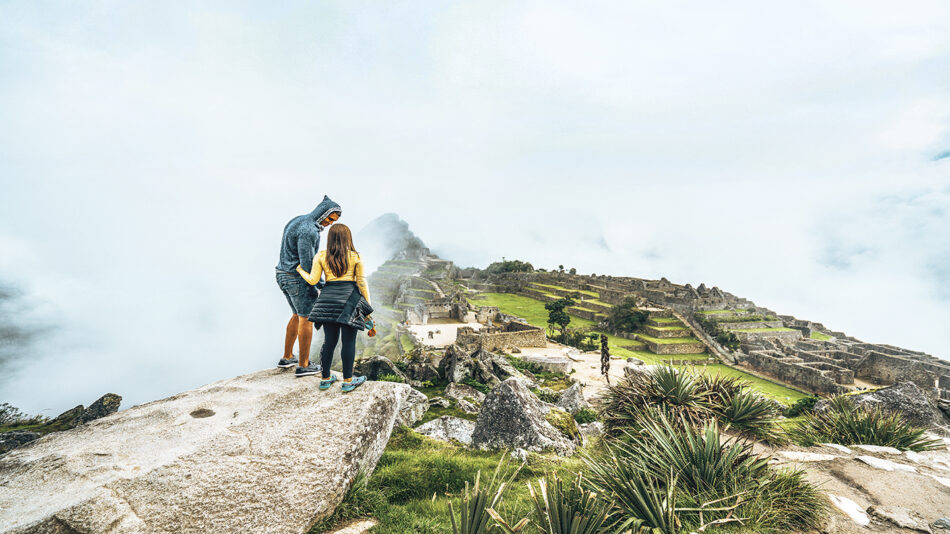 A man and woman standing on a rock overlooking a valley.