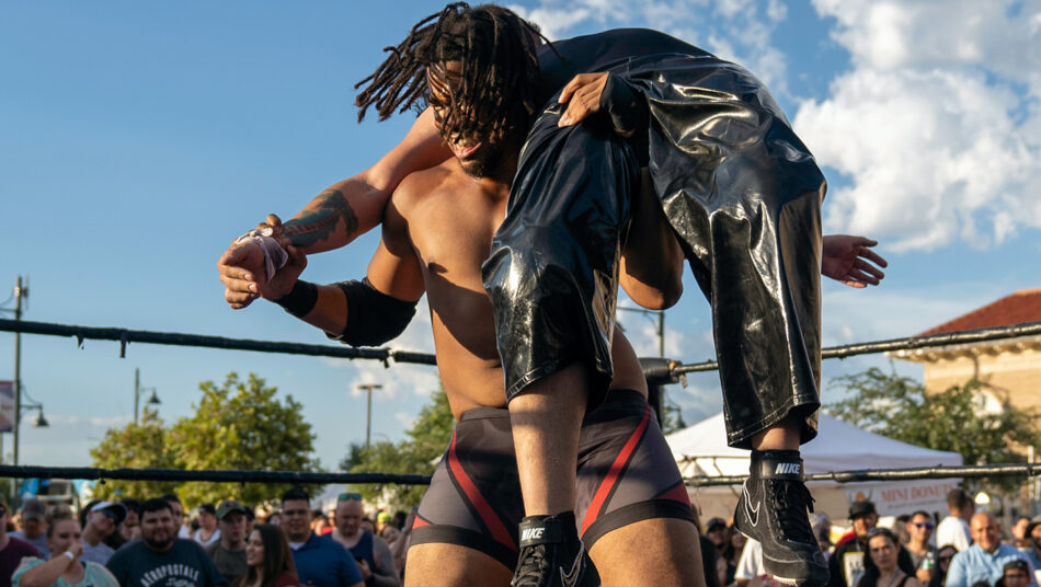 A wrestler is being carried by another wrestler in a wrestling ring.