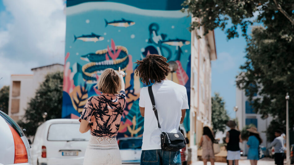 A couple exploring Cascais through art, admiring a vibrant mural in front of a car.