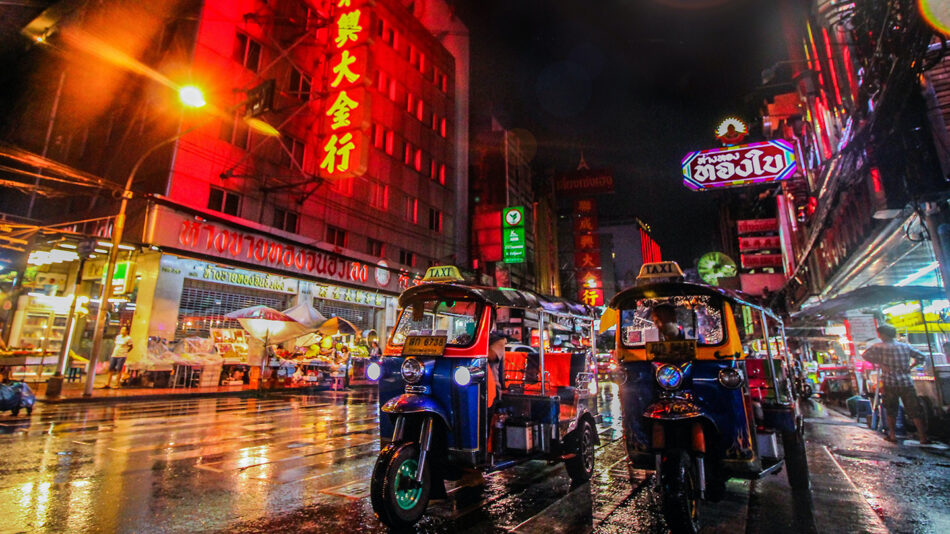 Two tuk tuks parked on a wet street in Thailand.