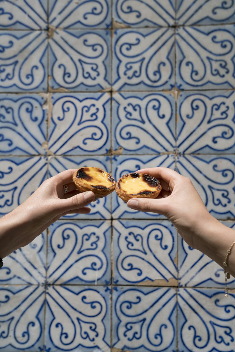 Two hands holding a piece of bread in front of a blue tiled wall.