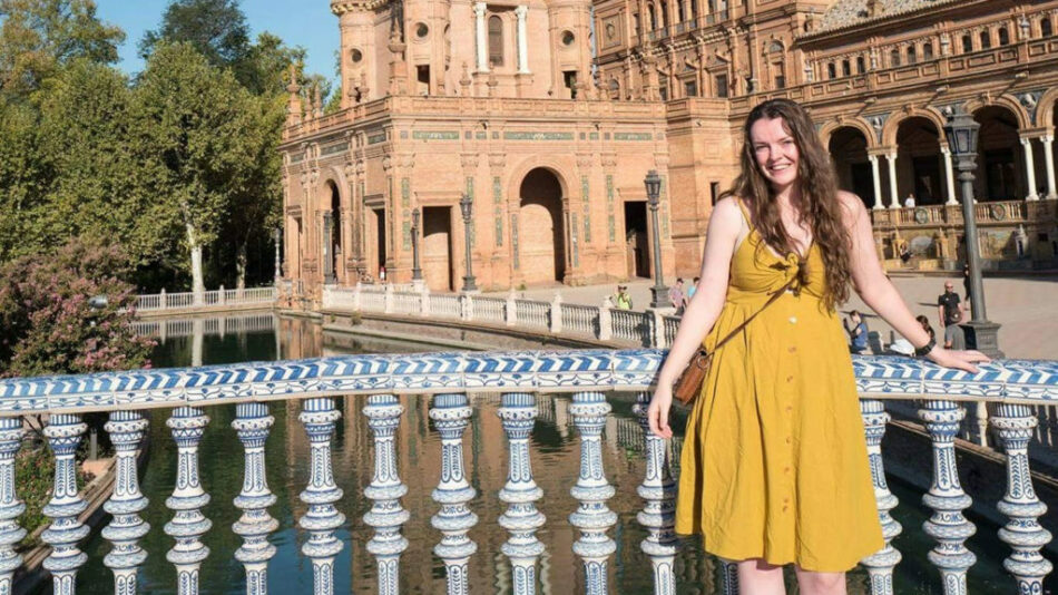 A woman in a yellow dress solo travel standing in front of an ornate building.