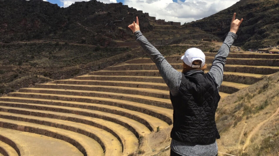 A woman on the Inca Trail with her arms raised in front of the ruins of Machu Picchu.