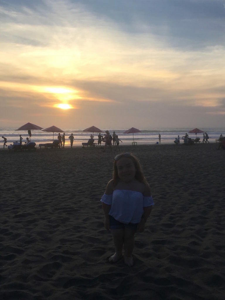 A little girl standing on the beach at sunset, filled with a passion for travel.