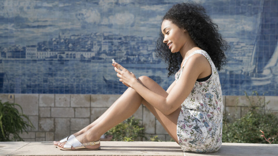 A young woman travelling alone on a ledge looking at her phone.