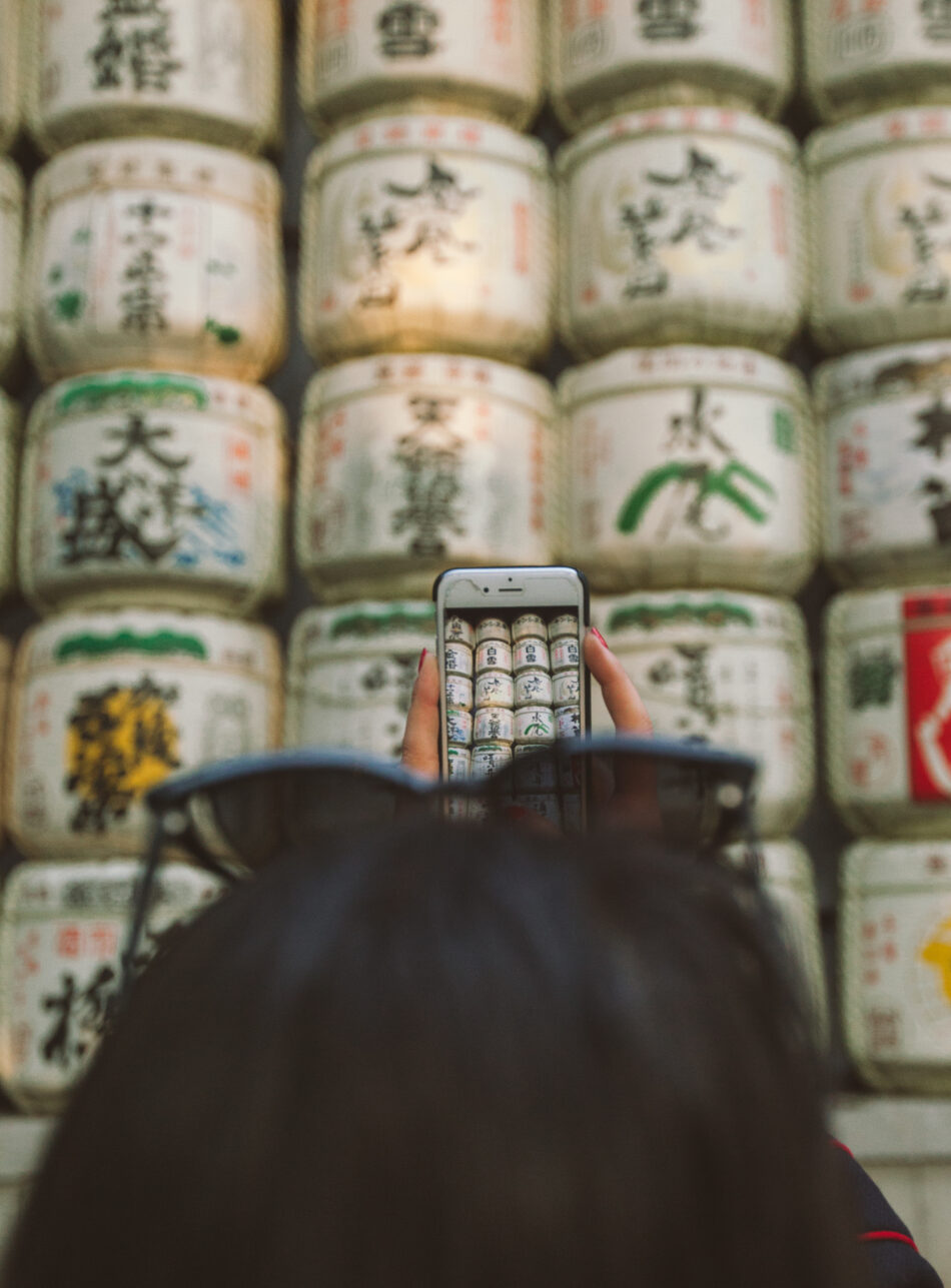 A person holding a cell phone in front of a wall of jars in Japan.