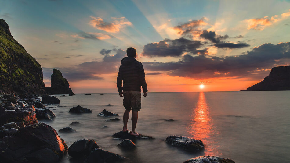 A man standing on rocks at sunset.