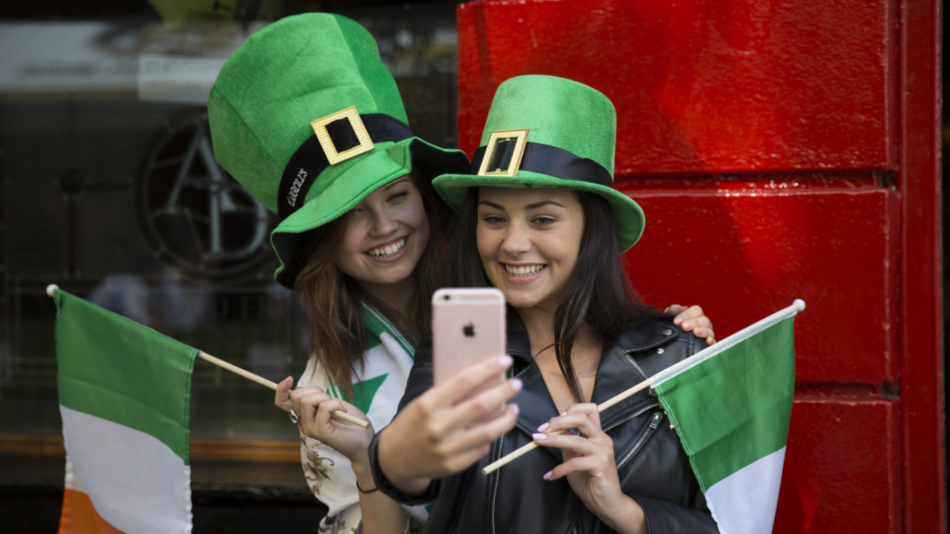 Two women in St. Patrick's Day hats joyfully taking a selfie during festive celebrations in 2023.