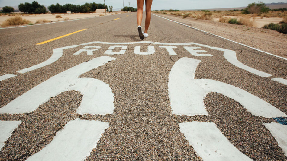 A woman is running down a road adorned with a Route 66 sign, showcasing one of the iconic things to do in North America.