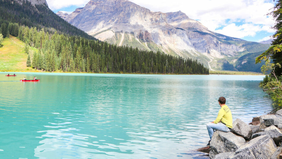 A woman is sitting on rocks near a picturesque lake in North America.