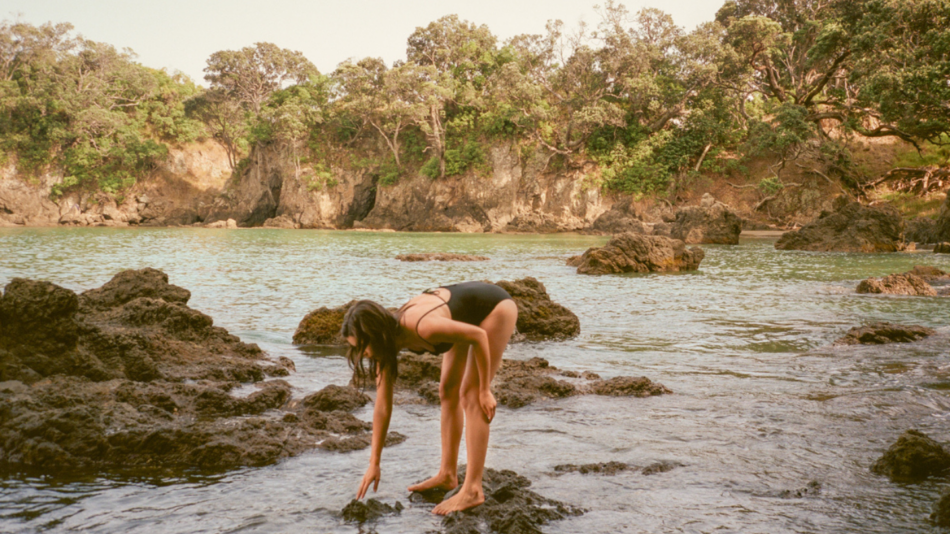 A woman in a bikini standing on rocks in the water.