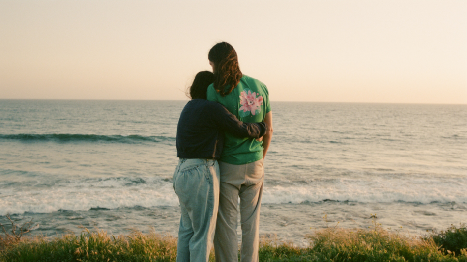 Two people standing on a hill overlooking the ocean.