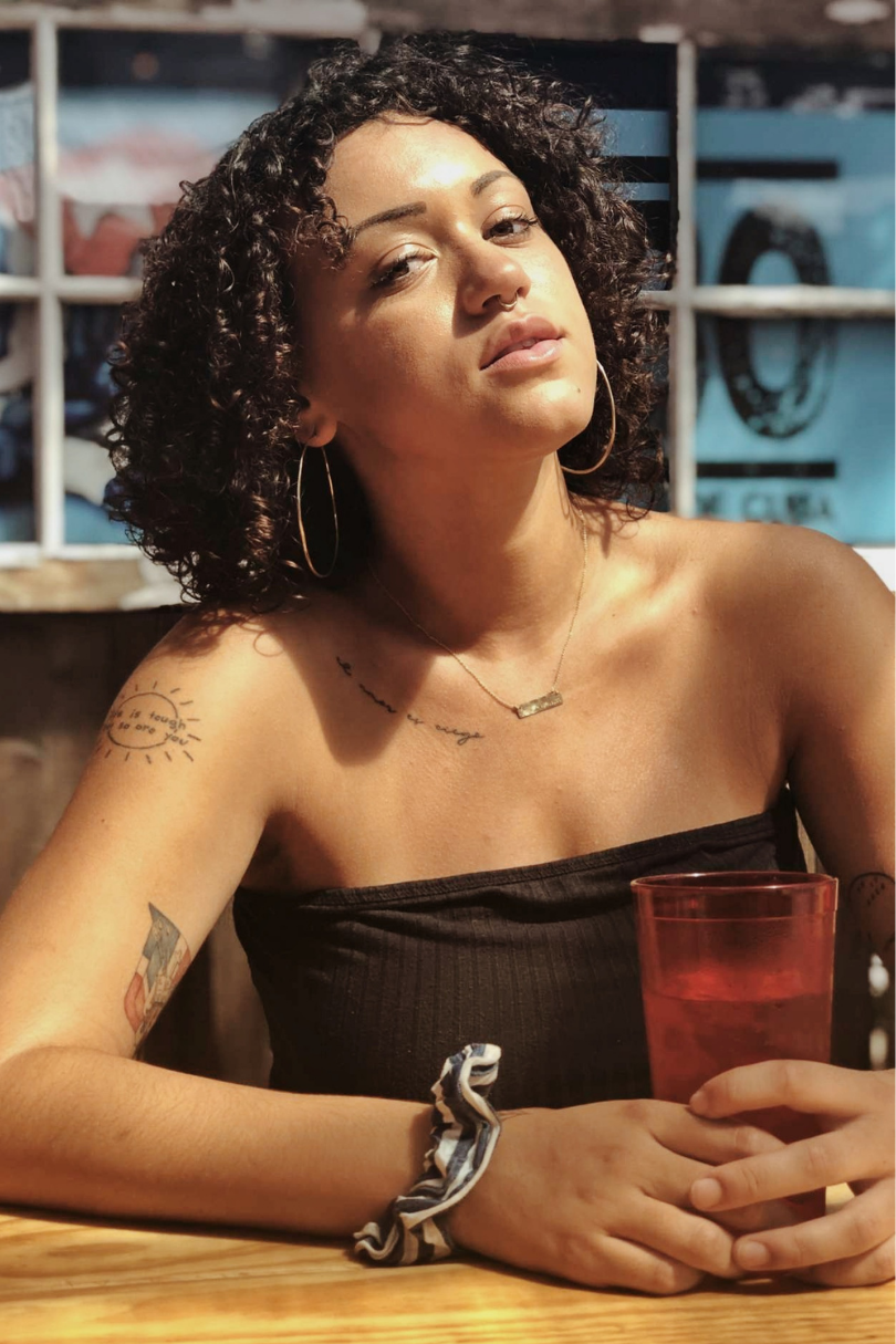 A woman with tattoos sitting at a table with a drink.