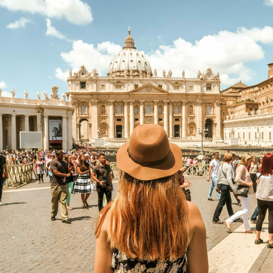 A woman in a hat is standing in front of st peter's square.