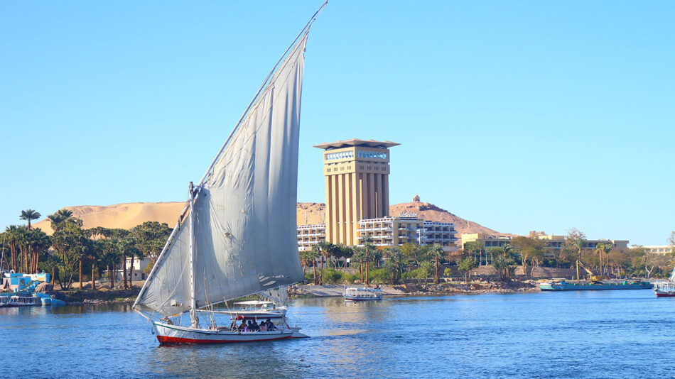 A boat sails down a river near a building.