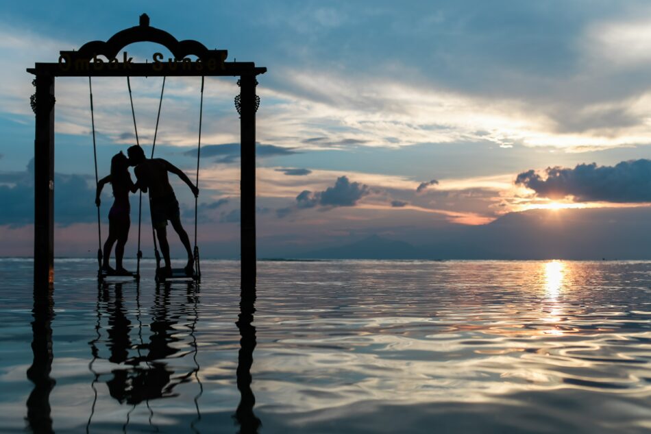 Two individuals seek life coach tips while enjoying a swing in the water during sunset.