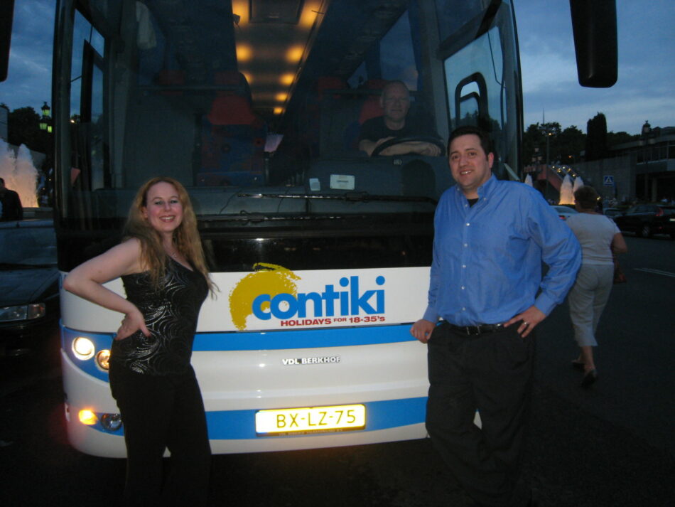 A man and a woman standing in front of a bus ready to travel around the world.