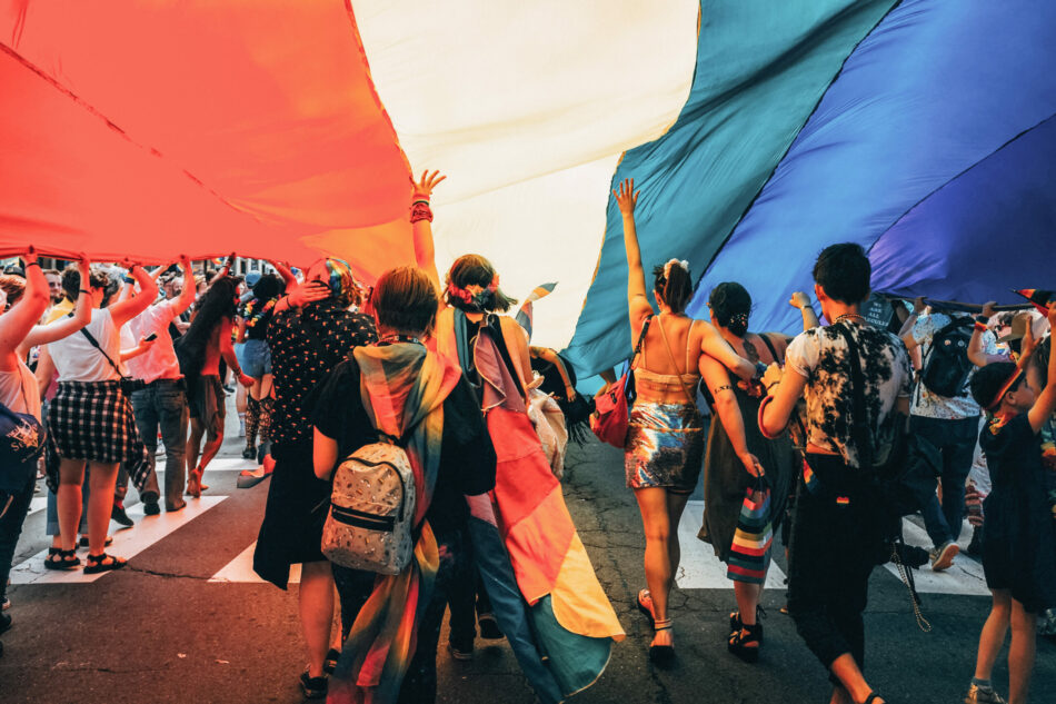 A group of LGBTQ+ individuals holding a rainbow flag in Spain.