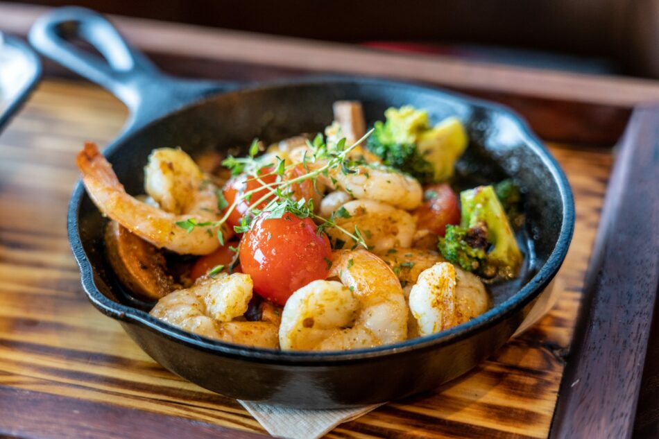 A skillet filled with shrimp and vegetables on a wooden table.