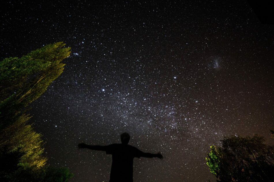 A man standing under the stars with his arms outstretched.